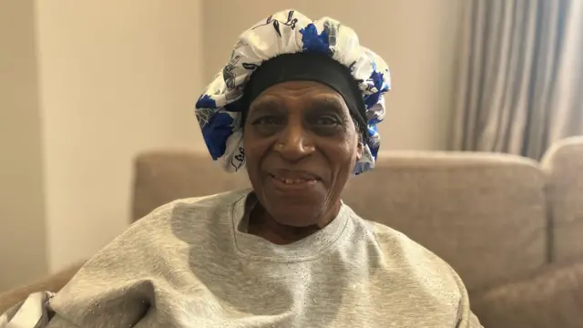 La residente Doris Robertson, con un sombrero suelto, sentada en una silla mirando a la cámara.