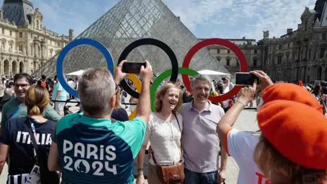 Visitors pose for pictures near the olympic rings in front of the Louvre Pyramid as part of the Paris 2024 Olympic Games