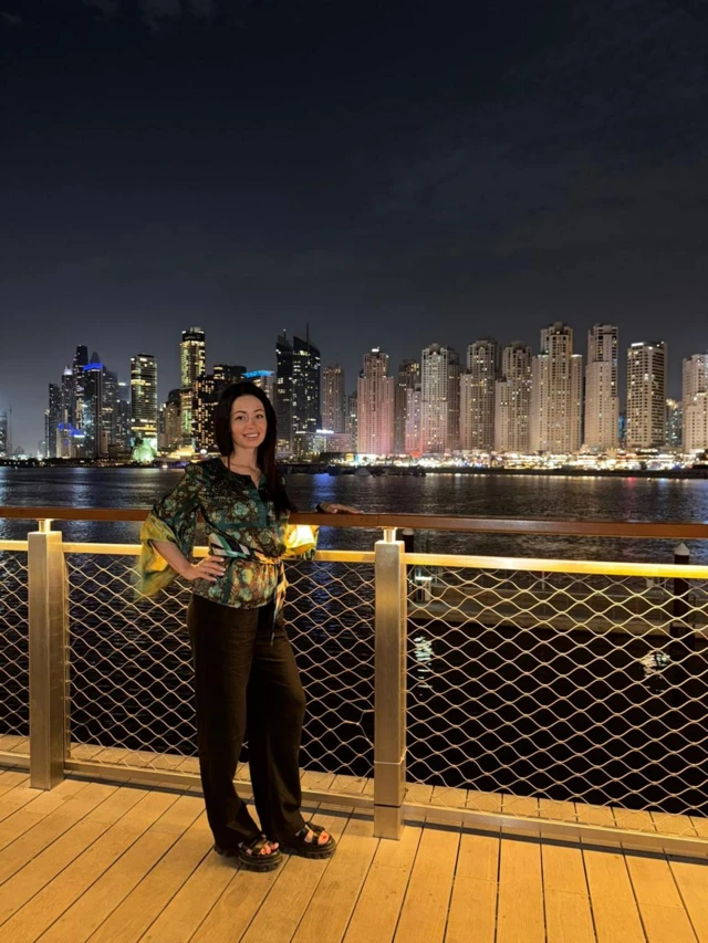 Девушка стоит на вечерней набережной на фоне небоскребов на другой стороне