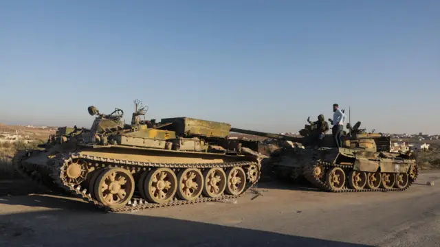 رجال يقفون على مركبة عسكرية مدمرة في مدينة معرة النعمان بمحافظة إدلب، بعد أن سيطر مقاتلو المعارضة على المدينة