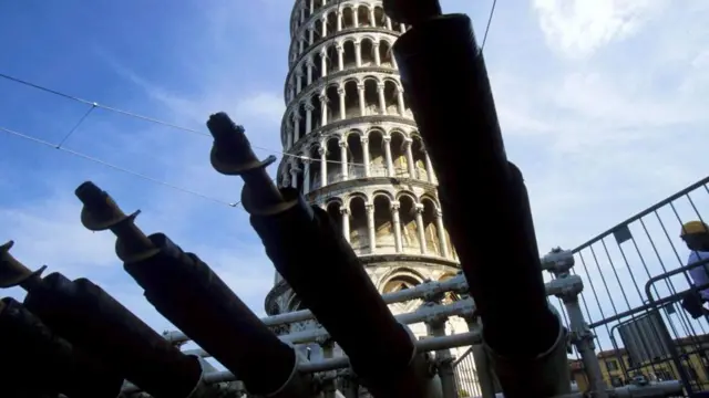 Uma fileira de máquinas de perfuração, com a Torre Inclinada de Pisa visível ao fundo.