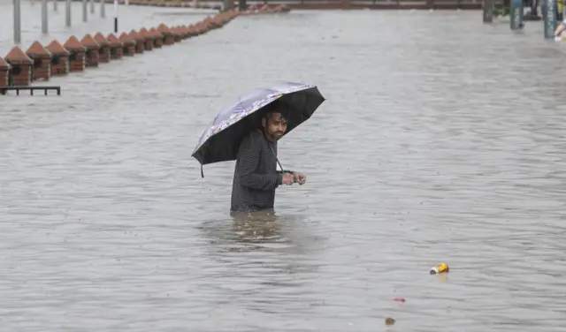 बर्खामा डुबानमा परेको ठाउँमा छाता बोकेर हिँड्दै एक व्यक्ति