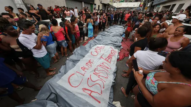Personas se encuentran junto a los cuerpos de sus familiares asesinados por la policía junto a una pancarta que dice "Claudio Castro, asesino y terrorista", el 29 de octubre de 2025.