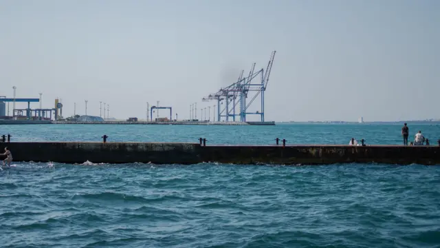 Чоловік на причалі дивиться на крани вдалині в одеському порту. У кадрі немає жодного корабля, що свідчить про те, наскільки порожні доки на тлі нещодавніх російських атак