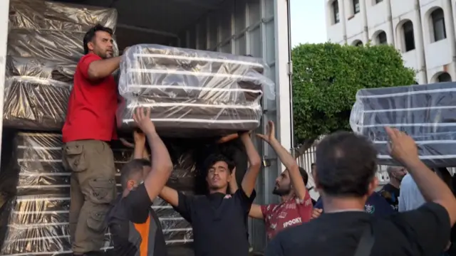 ટ્રકમાંથી ગાદલા ઉતારી રહેલા સ્વયંસેવકોની તસવીર 