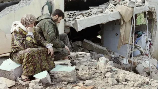 1996년 4월 28일 레바논 남부 시디키네에서 헤즈볼라 전사 한 명이 어머니와 함께 파괴된 집 옆에 앉아 있는 모습