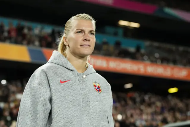 Ada Hegerberg entre sur le terrain avec un sweat à capuche gris et des cheveux blonds attachés en queue de cheval.