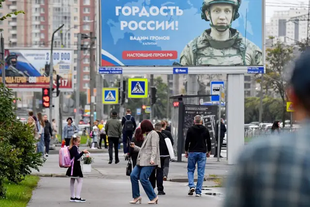 Улица Санкт-Петербурга с прохожими и огромным плакатом с военным и словами "Гордость России!"