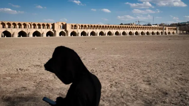 Bir adam, 2025 yılının başlarında, İran'ın tarihi İsfahan kentinde, Zayandeh Rud nehrinin kurumuş kıyısında dururken cep telefonunu kullanıyor 