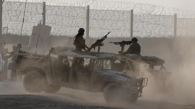 Солдаты Армии обороны Израиля стоят в двух открытых военных машинах с крупнокалиберными пулеметами возле огороженной колючей проволокой границы