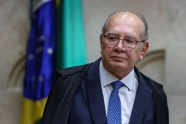 Gilmar Mendes usando toga. Há uma bandeira do Brasil atrás dele.