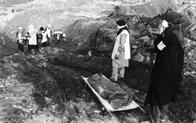 Women standing in front of a hole with a covered body next to it