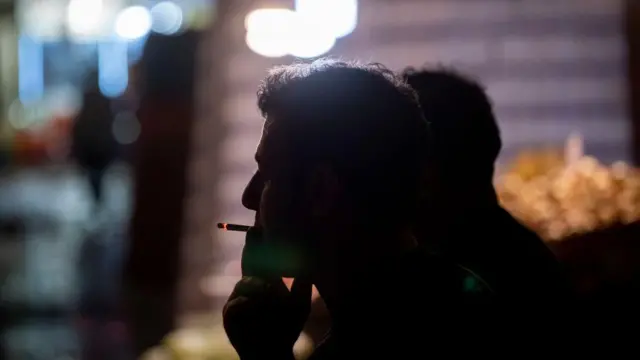 یک کارگر ایرانی در حال استراحت پس از یک روز کاری شبانه در یک بازار تعطیل در بوشهر، ایران، در ۸ آوریل ۲۰۲۴ در حال کشیدن سیگار است.