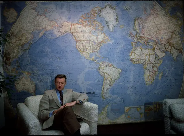 برژینسکی روی مبلی نشسته و پشت سرش نقشه جهان