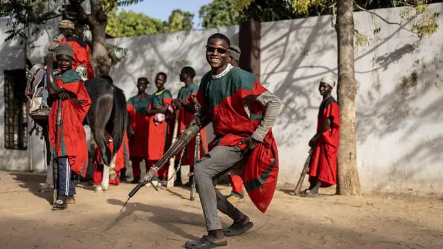 A royal hunter - wearing sunglasses and a red and green robe - poses with his gun