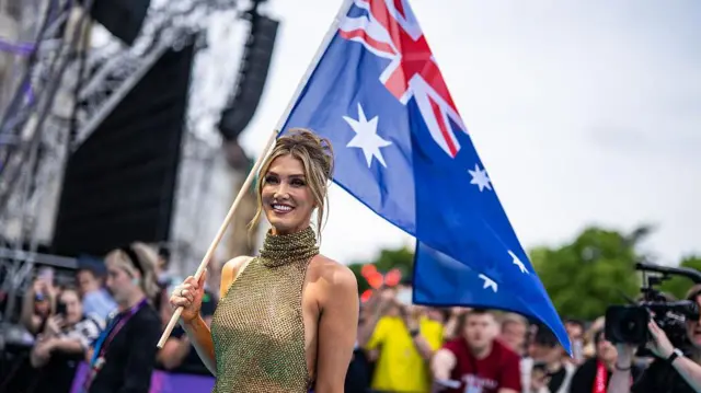 Delta Goodrem üzerinde kolsuz, altından bir elbiseyle Avustralya bayrağı taşıyor