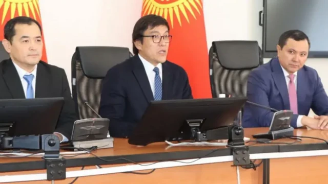 Эдил Байсалов икки томонида бошқа эркак сиёсатчилари билан, қора костюм, оқ куйлак устидан мовий галстук таққан, минбарда ўтириб сўзламоқда