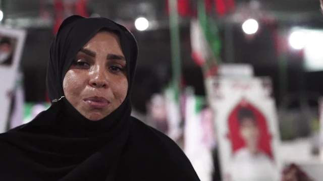 Masoumeh Mehran Shekhabadi, siyah bir çarşaf giymiş ve üzgün bir ifadeyle fotoğrafta görülüyor. Arkasında, mezarlıktaki mezarların başında yatan çocukların görüntüleri bulanık bir şekilde yer alıyor.
