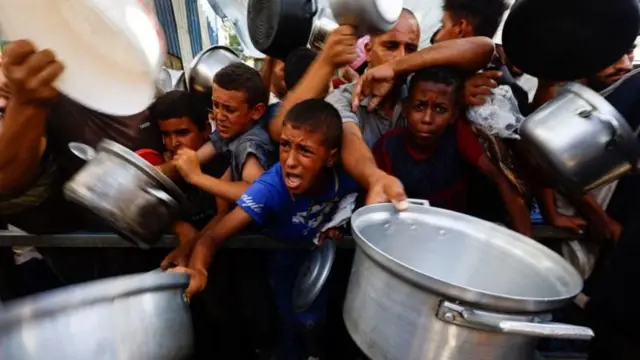 Crianças palestinas segurando por panelas à espera de ajuda humanitária em Gaza