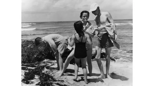 Robert Oppenheimer em momento de descontração com a família na praia em foto em preto e branco