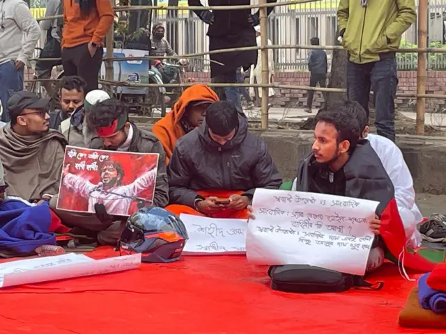 আজিজ সুপার মার্কেটের সামনে বিক্ষোভকারীদের কয়েকজনকে দেখা গেছে সকাল সাড়ে নয়টা নাগাদ