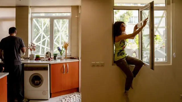 Tahran'da bir evde bir kadın camlara beyaz bant çekiyor.