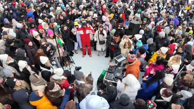 Багато людей у зимовому одязі стоять навколо діджея