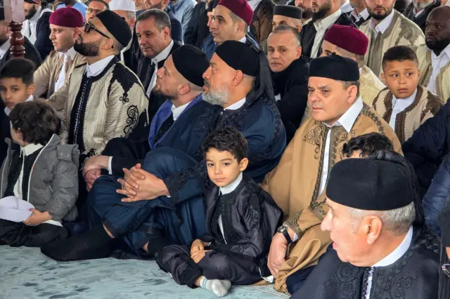 رئيس الحكومة الليبية عبد الحميد الدبيبة يجلس بجوار طفل أثناء حضوره صلاة عيد الفطر في ساحة الشهداء في العاصمة طرابلس