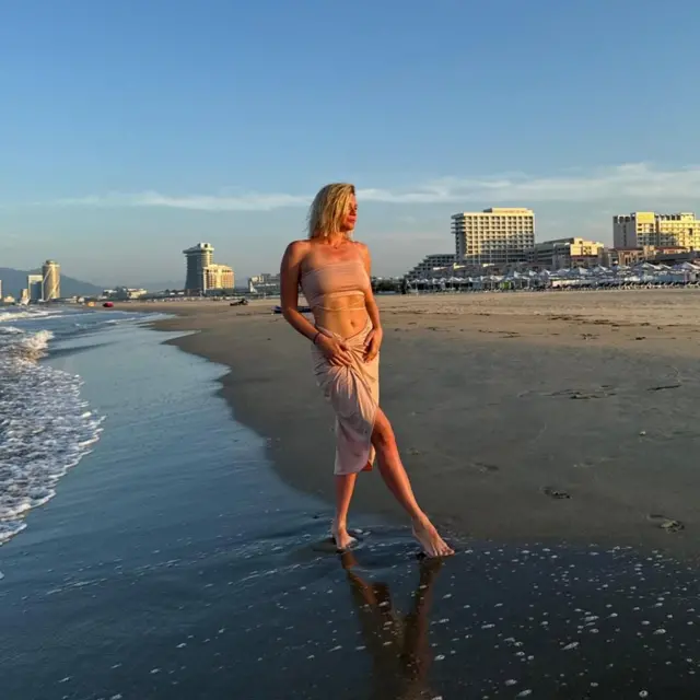 Anastasia posa en una playa en la que no se ven otras personas y de fondo tiene el complejo arquitectónico