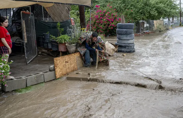 Sergio López arrastra una gran tabla de madera al frente de la casa rodante de su amigo para ayudar a desviar el agua de la inundación que corre durante la tormenta tropical Hilary en Thermal, California.