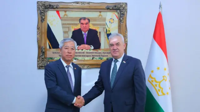 رحیم سعیدزاده، وزیر معارف و علم جمهوری تاجیکستان در دیدار با سفیر جدید چین، در حالی که دست می‌دهند مقابل دوربین عکس می‌گیرند، تصویر رئیس‌جمهور تاجیکستان و پرچم این کشور هم دیده می‌شود