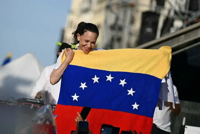La líder opositora venezolana María Corina Machado sostiene una bandera de Venezuela mientras sus partidarios se reúnen en la Puerta del Sol de Madrid el 18 de abril de 2026.