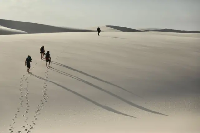 Turistas caminham em dunas 