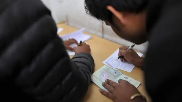 हातमा पासपोर्ट लिएर कुनै फारम भर्दै गरेका दुई व्यक्ति