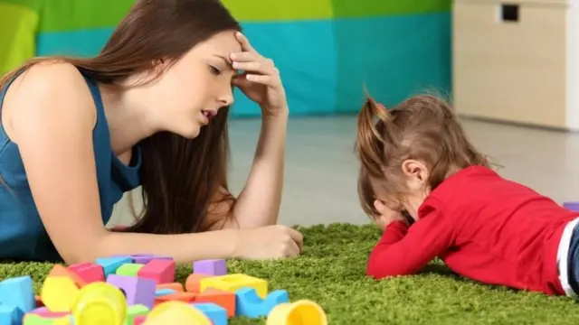 Mulher com a mão na testa conversando com uma criança que está fazendo birra