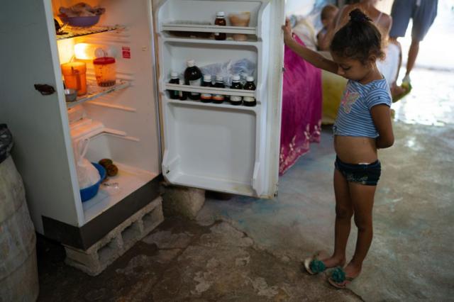 Menina segurando porta de geladeira aberta
