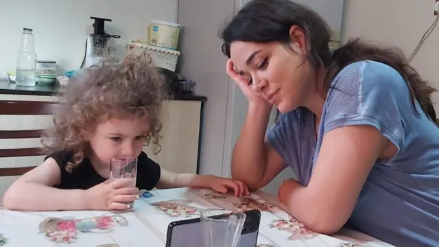 Nazanin and her youngest daughter, Delsa, looking at a phone proped up by a glass on a kitchen table