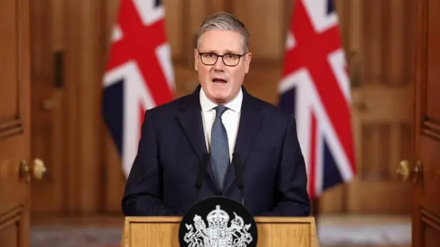 木製の壁やドア、イギリス国旗に囲まれて話すスターマー氏