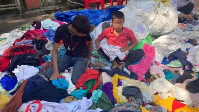 दान किए गए कपड़ों में अपने नाप के कपड़े तलाशते बच्चे