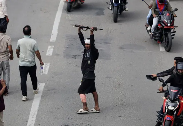 Muškarac sa zavojem na glavi na ulici drži pušku visoko podignutu u vazduh