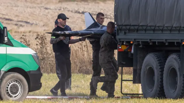 Três homens carregam um drone para dentro de um caminhão.