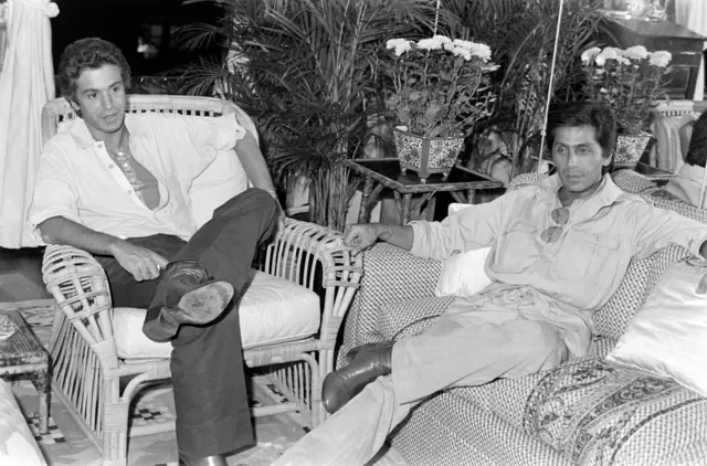 İki erkek siyah beyaz bir fotoğrafta ayrı koltuklarda oturuyor. İkisi de ayak ayak üzerine atmış