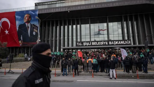 Şişli Belediyesi binası önünde kalabalık, önde bir polis, arkada Türk bayrağı ve Atatürk'ün resmi