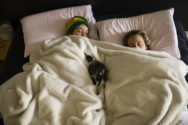 Ave acostada en la cama junto a la madre y uno de los niños