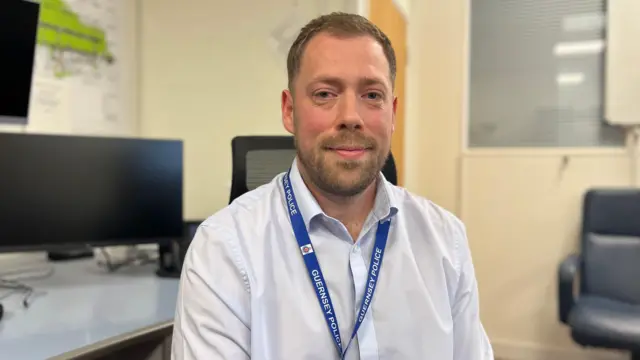 Thomas Lowe aparece en la foto con una camisa blanca abotonada. Tiene el pelo castaño corto y barba. Lleva un cordón azul de la Policía de Guernsey.