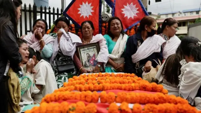 जेन जी आन्दोलनमा ज्यान गुमाएका एक युवकको शव राखिएको पेटिकाअगाडि उनका भावविह्वन आफन्तहरू, पृष्ठभूमिमा नेपाली झण्डाहरू छन् 