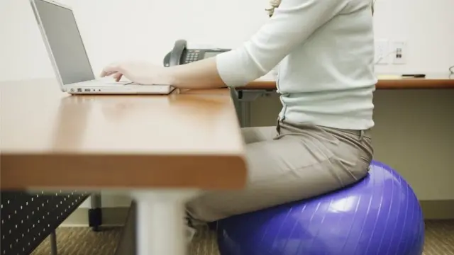 Mujer sentada sobre un balón suizo en una oficina.