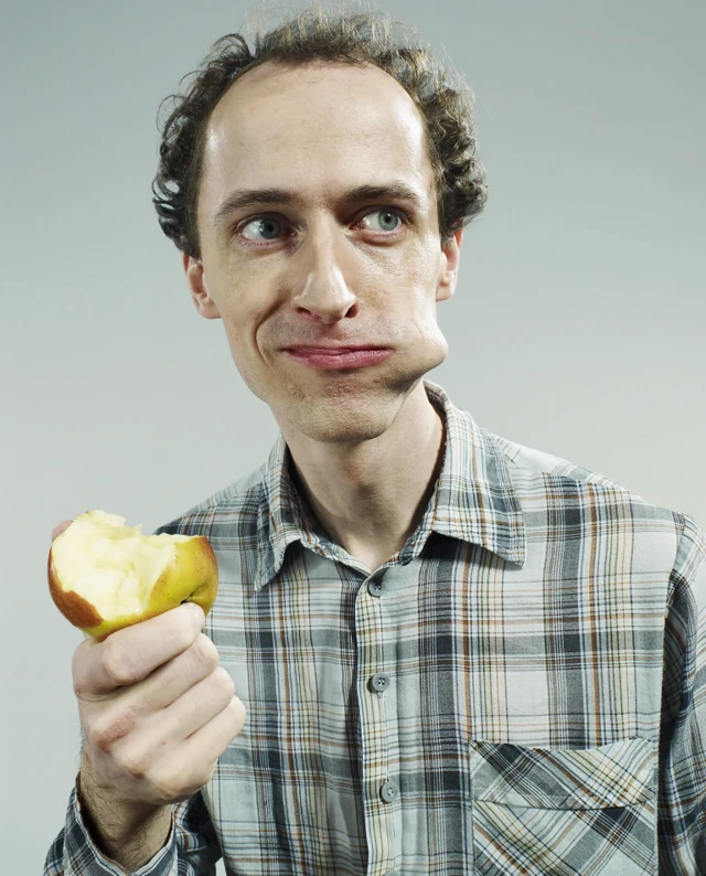 체크무늬 셔츠를 입은 남성이 사과를 먹고 있다