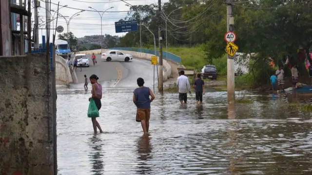 Pessoas caminham por rua alagada na periferiamines f12betSão Paulo