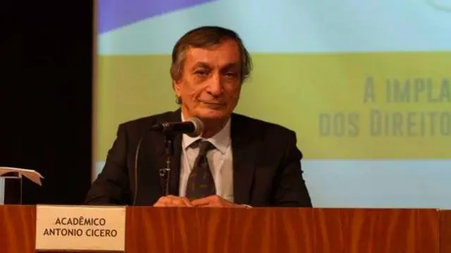 Antonio Cícero sentado à mesa durante palestra